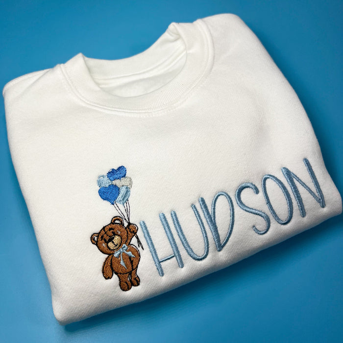White jumper with teddy bear holding heart balloons embroidered on the front along with a name