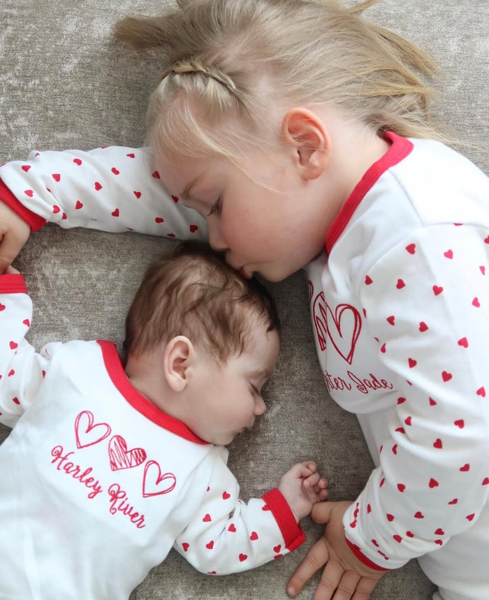 Two children wearing matching pajamas with red hearts and names.
