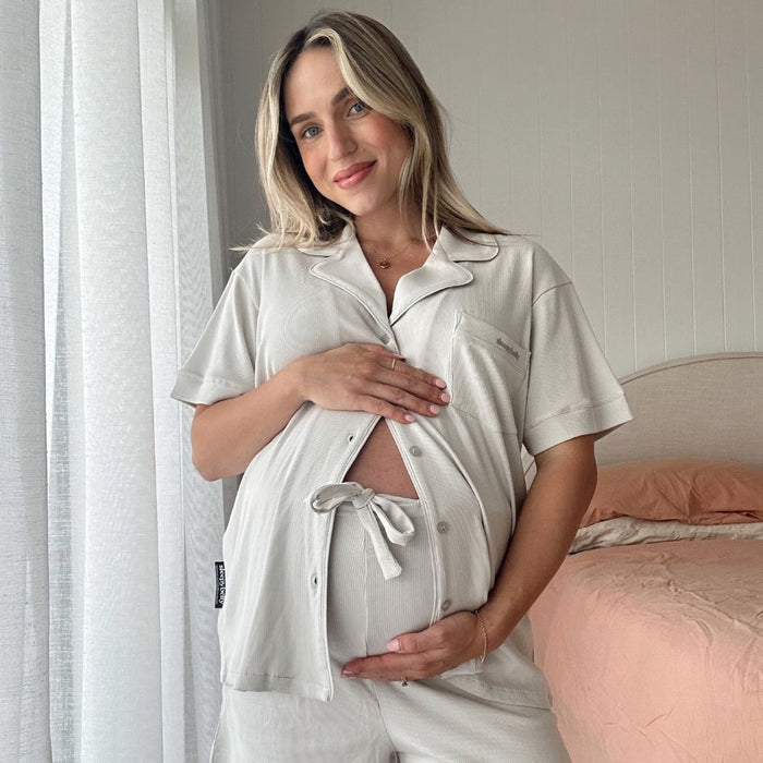 Pregnant woman wearing the stone 3-piece maternity pyjama set with tie-front top framing her bump