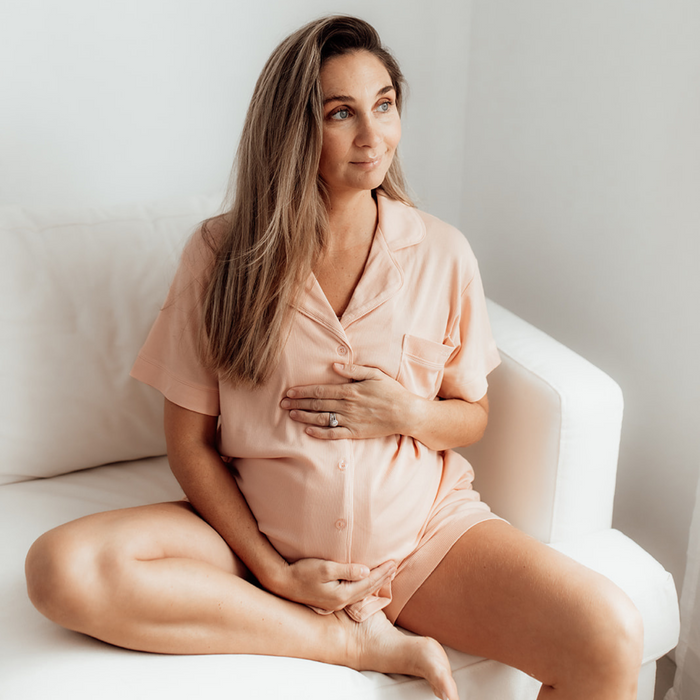 Pregnant woman relaxing on a sofa in the peach short-sleeve Sleepybelly maternity pyjama set