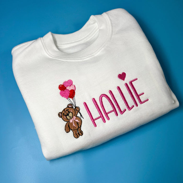 White sweatshirt with a bear holding heart balloons with child’s name embroidered on the front