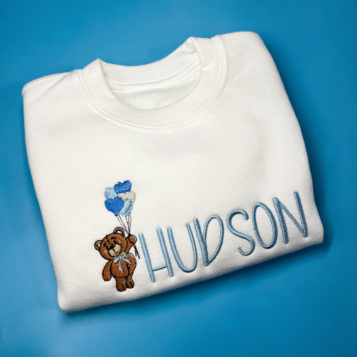 White jumper with teddy bear holding heart balloons embroidered on the front along with a name