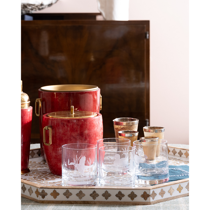 A bar-themed product display featuring a red and gold ice bucket set and matching clear glass tumblers with gold trim, arranged on a decorative tray in an indoor setting.