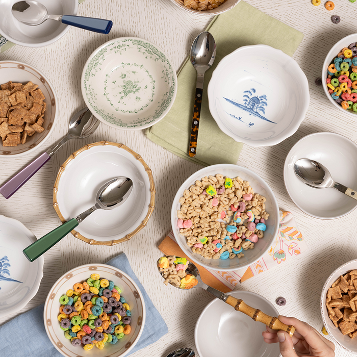 Celery green linen napkin under white bowls with colorful cereals and spoons on a light wood table.