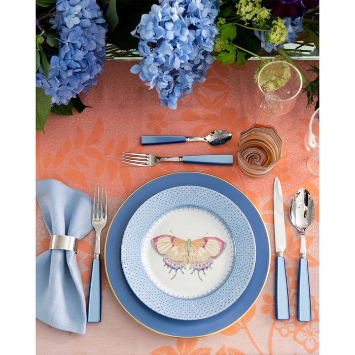 Blue cocktail plate with lace pattern and butterfly accent on white center, paired with blue flatware and napkin on coral.