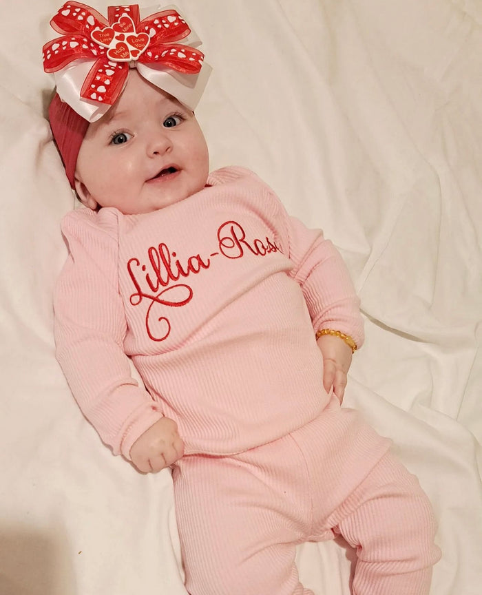 Baby girl wearing pink ribbed tracksuit with lillia rose embroidered on the front in red