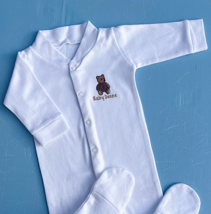 White baby onesie with a teddy bear design and 'Baby Denne' text on a blue background