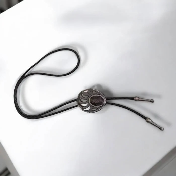 Two bear paw bolo ties with black braided leather cords: silver-tone faux turquoise bear claw slider and black stone bear paw pendant with antique metal tips.