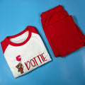 A set of children's pyjamas with a white top that has a red bear graphic and the name 'Dotty' written on it, and red pants with a small bear design.
