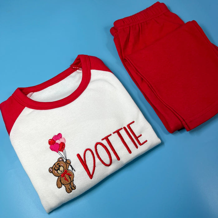 A set of children's pyjamas with a white top that has a red bear graphic and the name 'Dotty' written on it, and red pants with a small bear design.