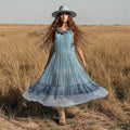 woman wearing in field with fedora and boots Blue Sleeveless Tiered A-Line Maxi Dress with floral rosettes, crochet lace hem, and boho style / women's / large