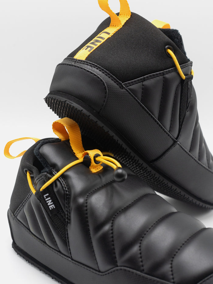 Black snow boots with yellow accents on a light gray background
