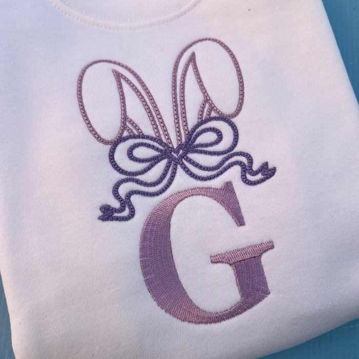 White jumper with embroidered bunny ears, a large bow and the letter G