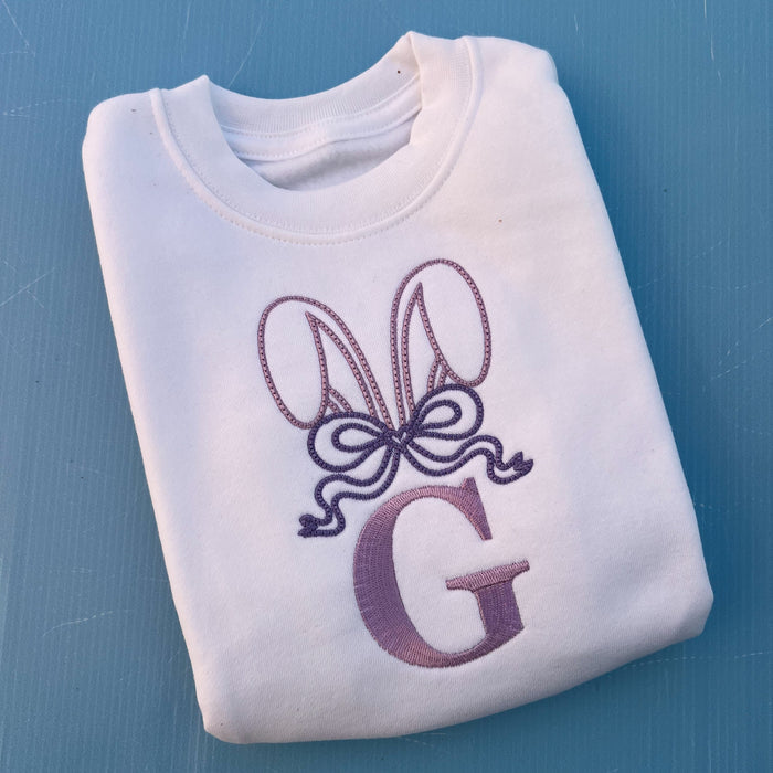 White jumper with embroidered bunny ears, a large bow and the letter G