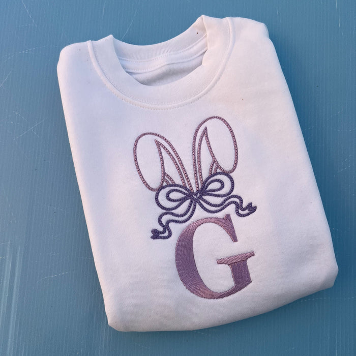 White jumper with embroidered bunny ears, a large bow and the letter G