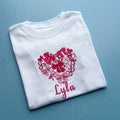 White shirt with pink floral heart design and 'Lyla' text on a blue surface