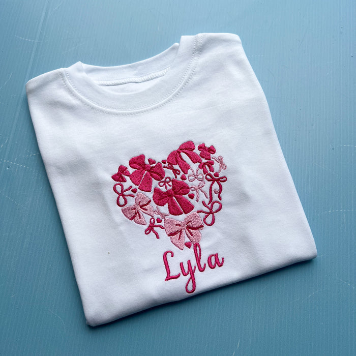 White shirt with pink floral heart design and 'Lyla' text on a blue surface