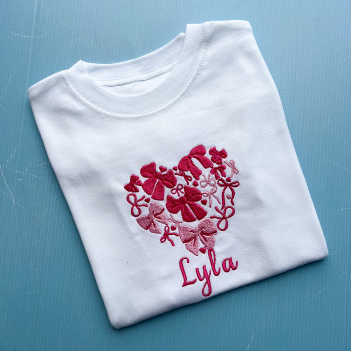 White t-shirt with red heart design and 'Lyla' text on a blue surface