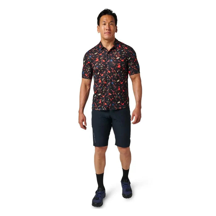 Man wearing a patterned shirt and dark shorts on a white background