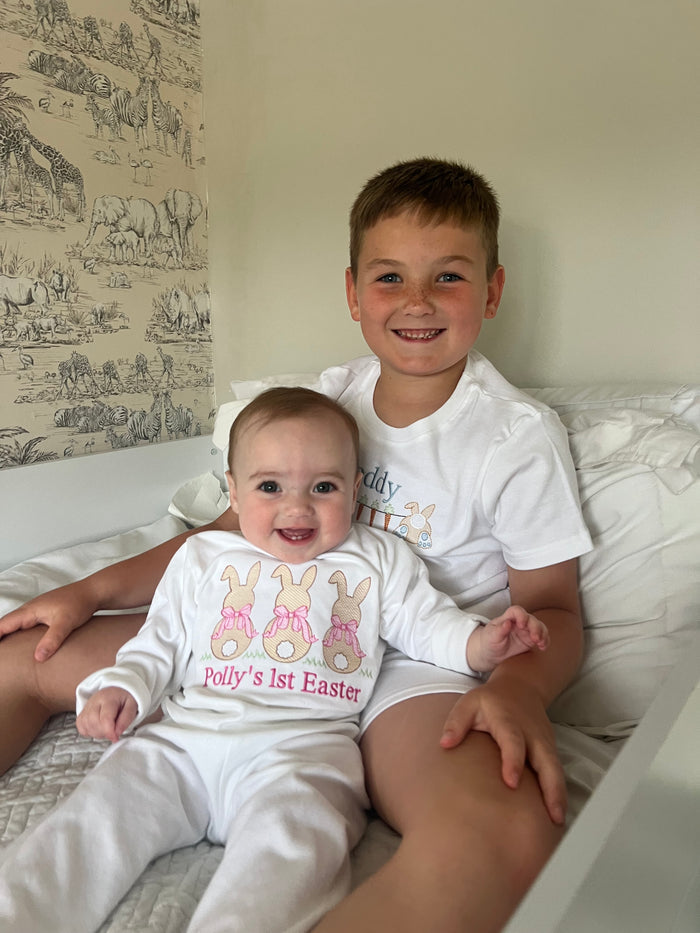 Two children, a brother and a baby sister, wearing matching Easter-themed outfits on a couch.