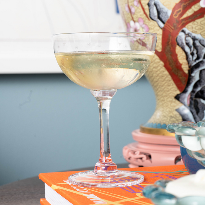Clear glass champagne coupe with a delicate stem filled with pale champagne on a wooden table.