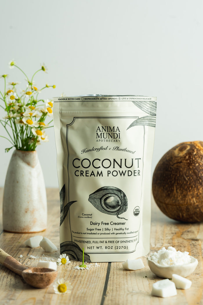 Anima Mundi coconut cream powder packaging on a wooden surface with coconuts and flowers.