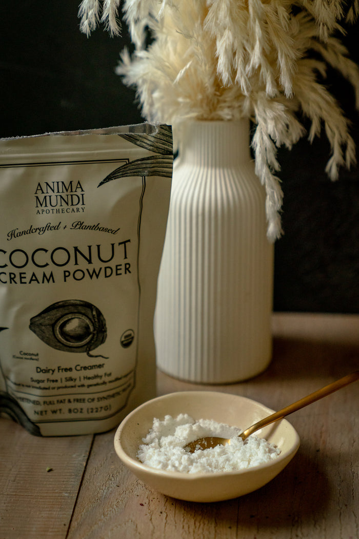 Coconut cream powder from Anima Mundi Apothecary in a bowl with a gold spoon on a wooden surface.