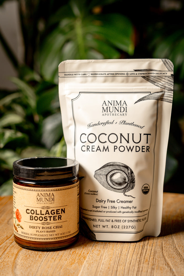 Anima Mundi Coconut Cream Powder package and Collagen Booster jar on a wooden surface with greenery in the background