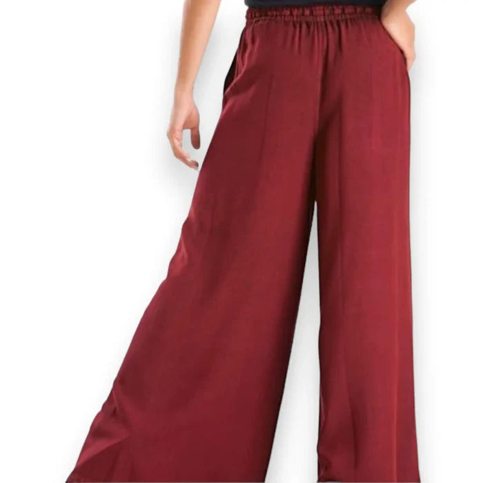 Woman wearing burgundy red wide-leg palazzo pants on a boho city stroll, styled with a relaxed top and sandals for a breezy streetwear look.