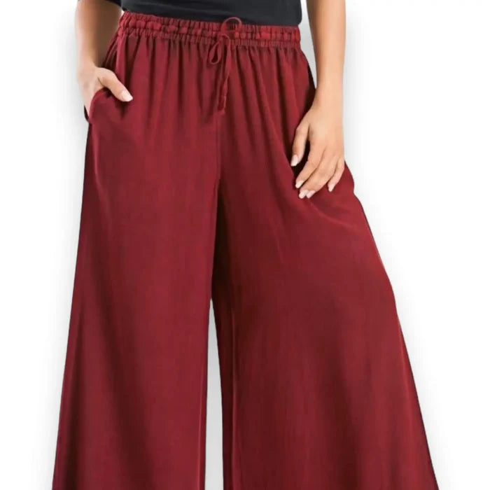 Woman wearing burgundy red wide-leg palazzo pants on a boho city stroll, styled with a relaxed top and sandals for a breezy streetwear look.