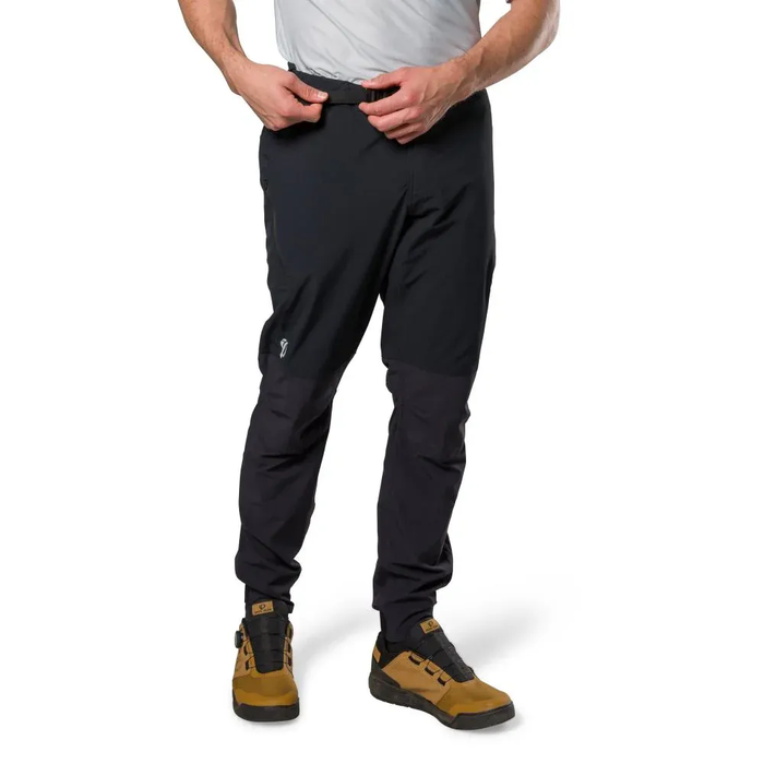 Person wearing black pants and brown shoes on a white background