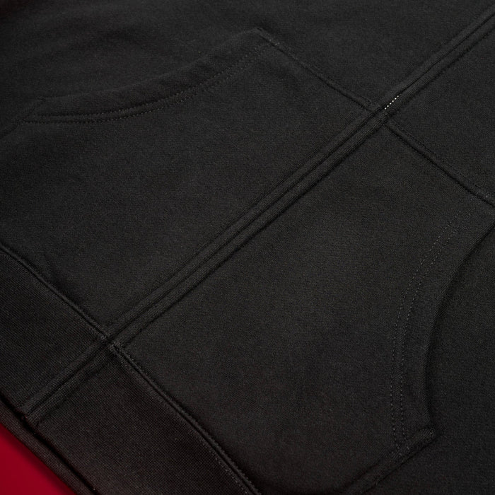 Close-up of a dark charcoal gray garment with visible seam stitching, laid against a red background.