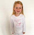 Young girl wearing a white long-sleeve shirt with text and floral design on a plain background