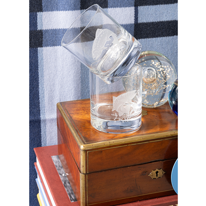 Set of four clear rocks glasses with etched fly fishing insect designs on wooden box background.