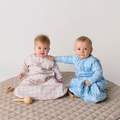 Two babies sitting wearing a Sleepybelly Infant Sleeping Bag in colours blue and grey, one is wearing a 2.5 TOG baby sleep sack with sleeves attached for 3-12 month olds. The other is wearing a 1.0 TOG baby sleep sack with sleeves attached for 3-12 month olds.