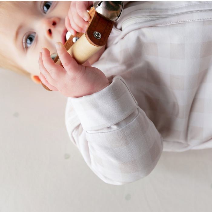 Baby chewing a wooden toy while wearing the linen grey gingham infant sleep sack with fold-over cuff