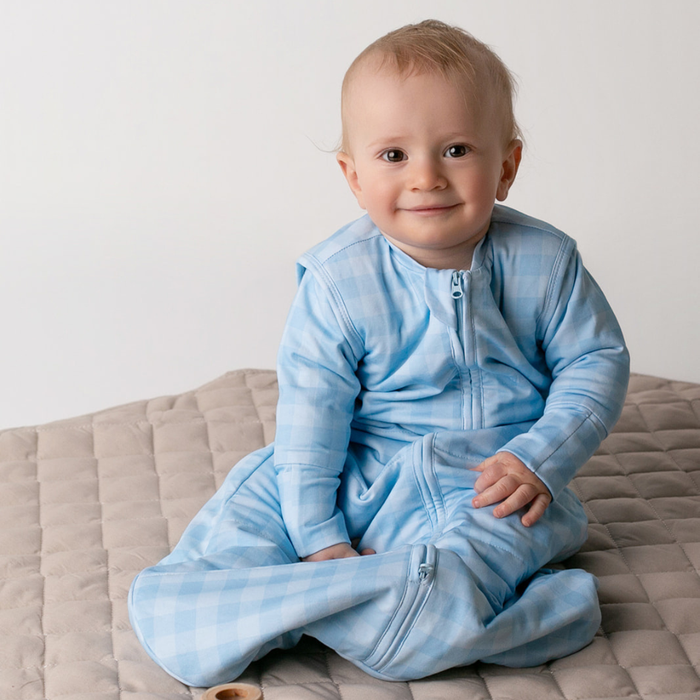 Smiling baby sitting up in the blue gingham infant sleep sack with sleeves on