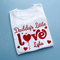 Folded white t-shirt with red text and hearts on a blue background