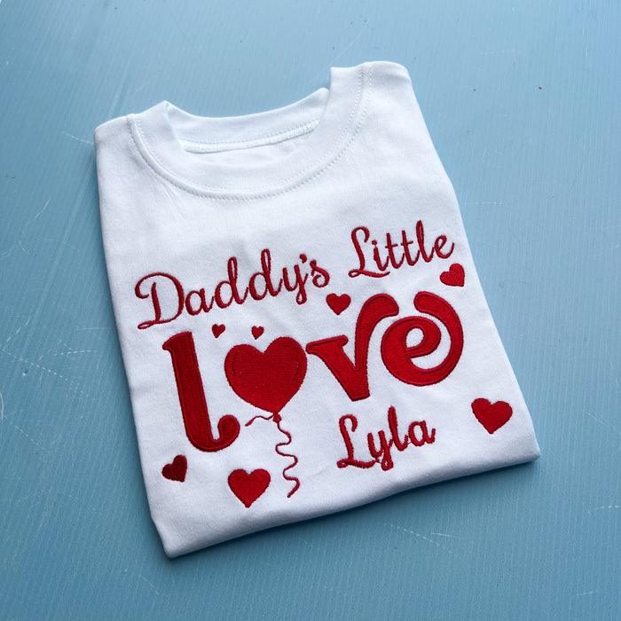 Folded white t-shirt with red text and hearts on a blue surface