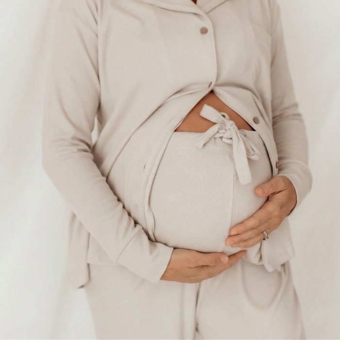 Close-up of a mum-to-be cradling her bump in the buttoned linen grey long sleeve maternity pyjama top