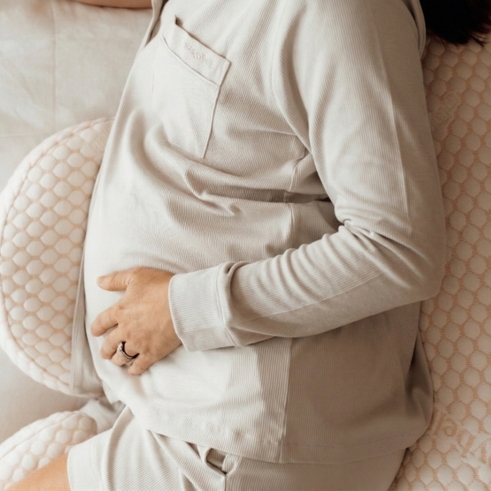 Pregnant woman lying back with hands on her bump in the linen grey long sleeve maternity pyjama top