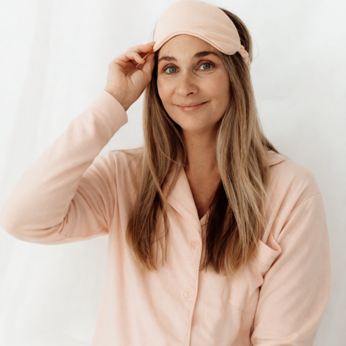 Smiling woman lifting a matching sleep mask while wearing the pink long sleeve maternity pyjama top