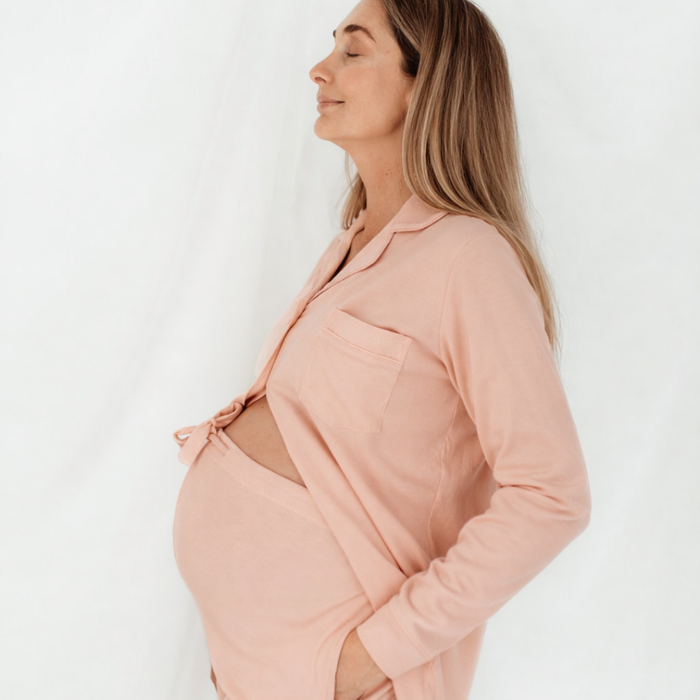 Side profile of a pregnant woman wearing the pink long sleeve maternity pyjama top open over her bump