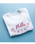 White sweatshirt with 'Millie' embroidered on it along with a love letter chain against a blue background