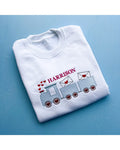 White sweatshirt with embroidered design and name 'HARRISON' on a blue background