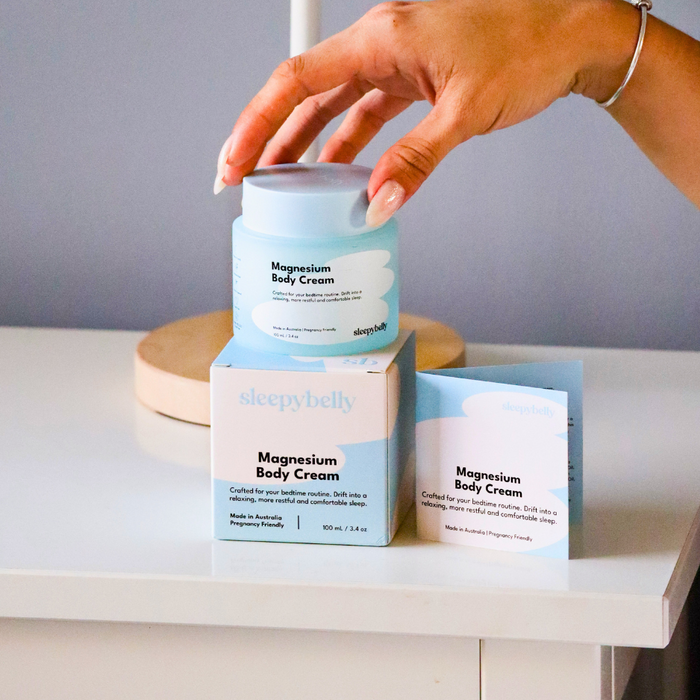 Hand reaching for a tub of Sleepybelly Magnesium Body Cream stacked on its packaging boxes