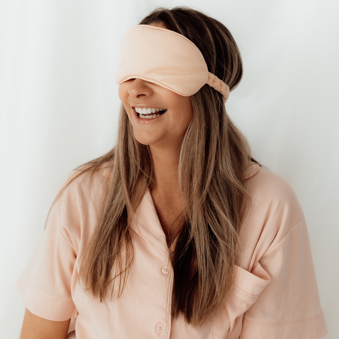 Smiling woman wearing the blush pink Sleepybelly matching eye mask with pink maternity pyjamas