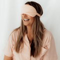 Smiling woman wearing the blush pink Sleepybelly matching eye mask with pink maternity pyjamas