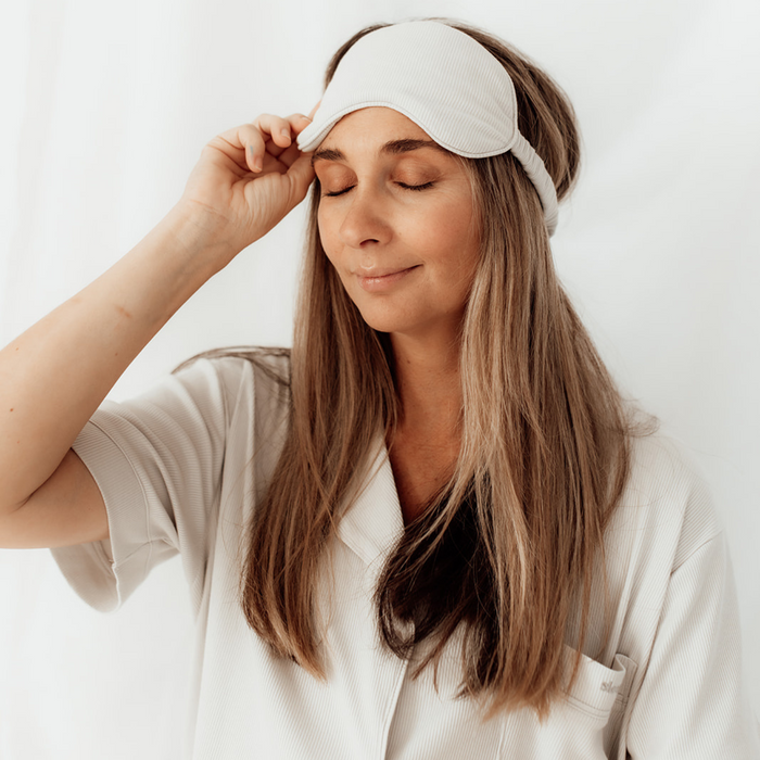 Woman lifting the grey Sleepybelly matching eye mask, paired with white maternity pyjamas