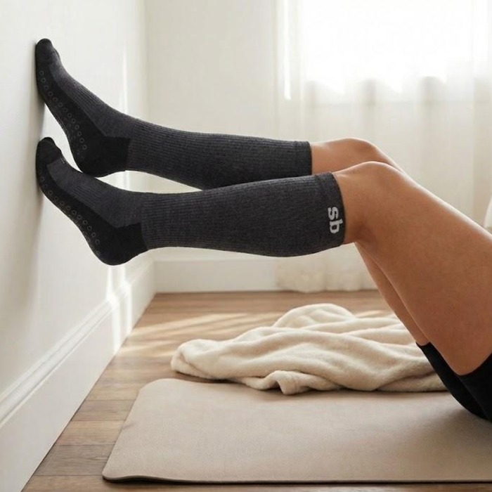 Legs resting up the wall in charcoal maternity compression socks to ease swelling